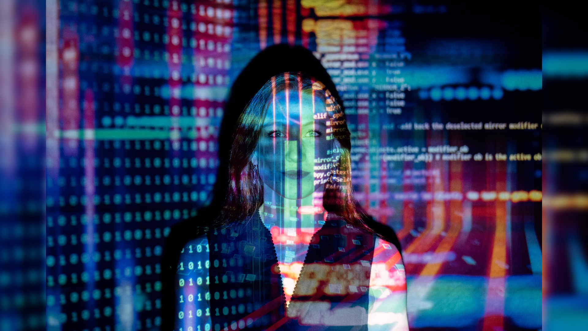 An image depicting the top half of a woman facing the camera while her face and upper body are covered in projected lights of code, symbolizing a connection between humanity and technology